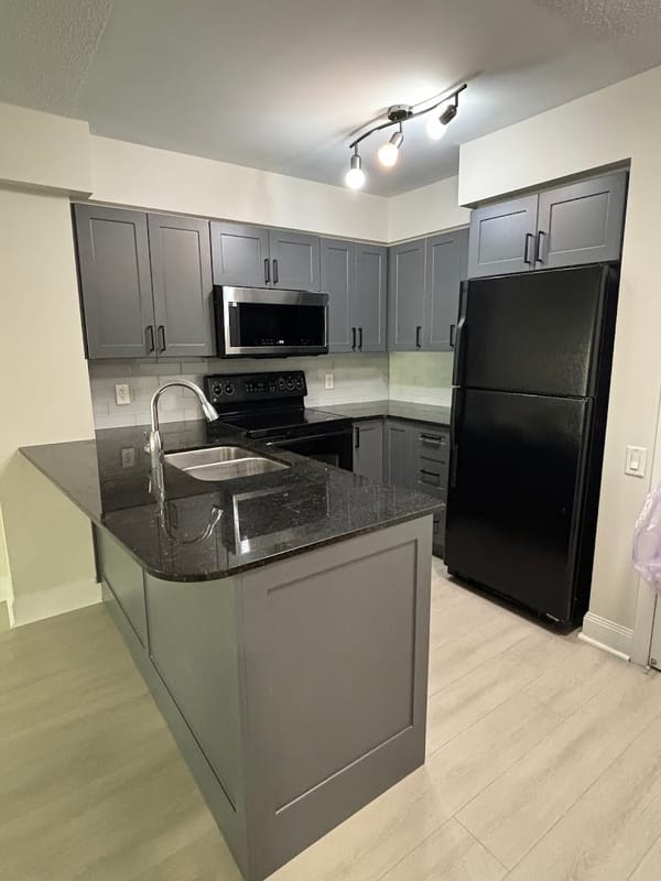 Renovated condo kitchen with grey shaker cabinets and dark stone counters