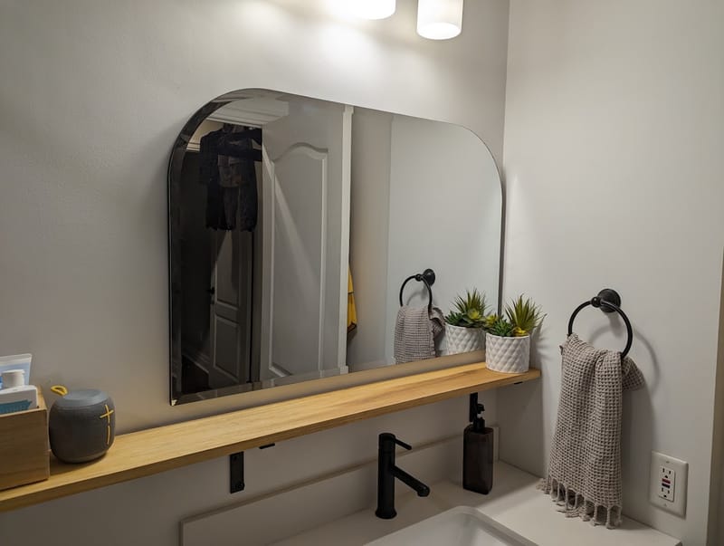 Arched mirror and wood shelf mounted above a bathroom vanity